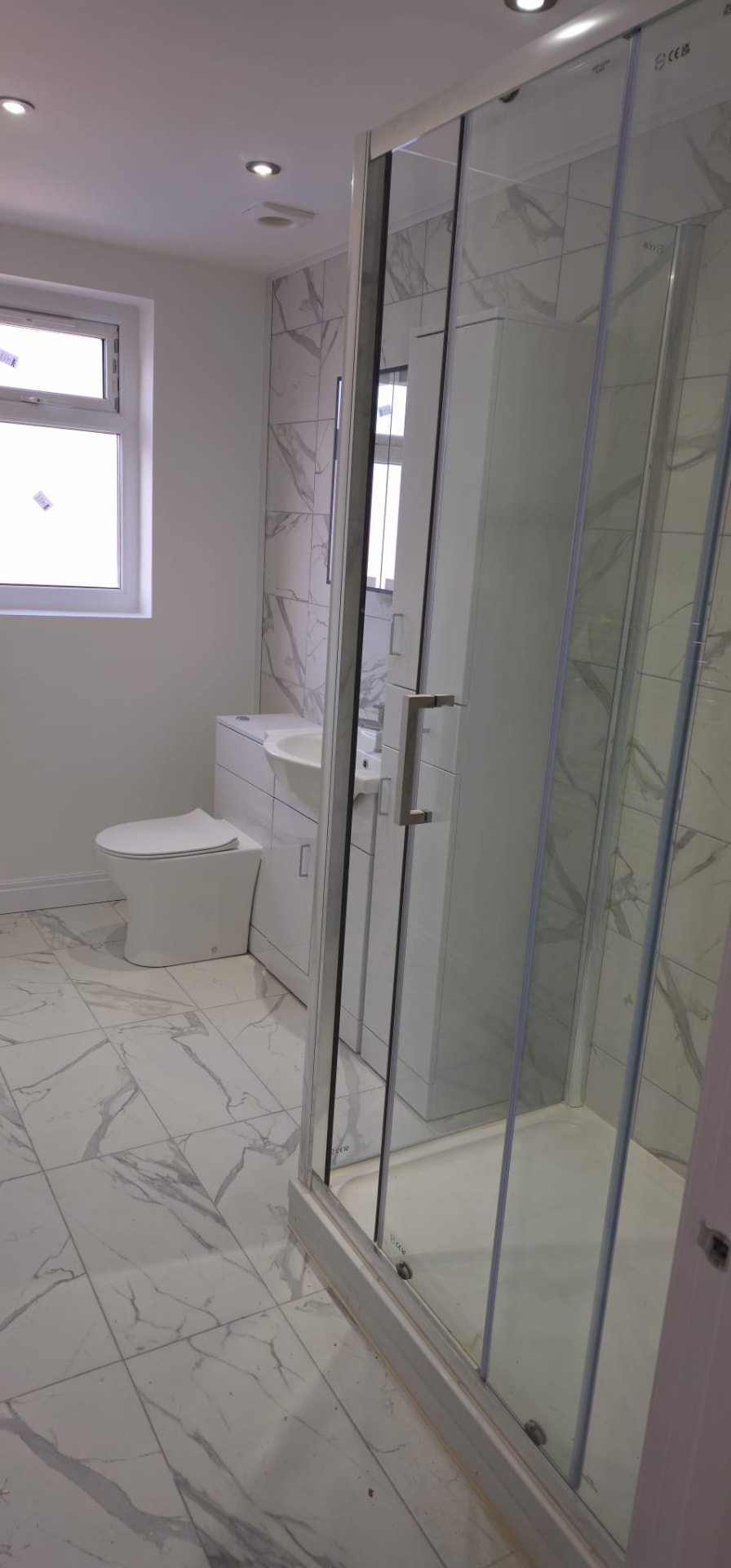 Finished modern bathroom with marble-effect tiles and glass shower cubicle, Leeds