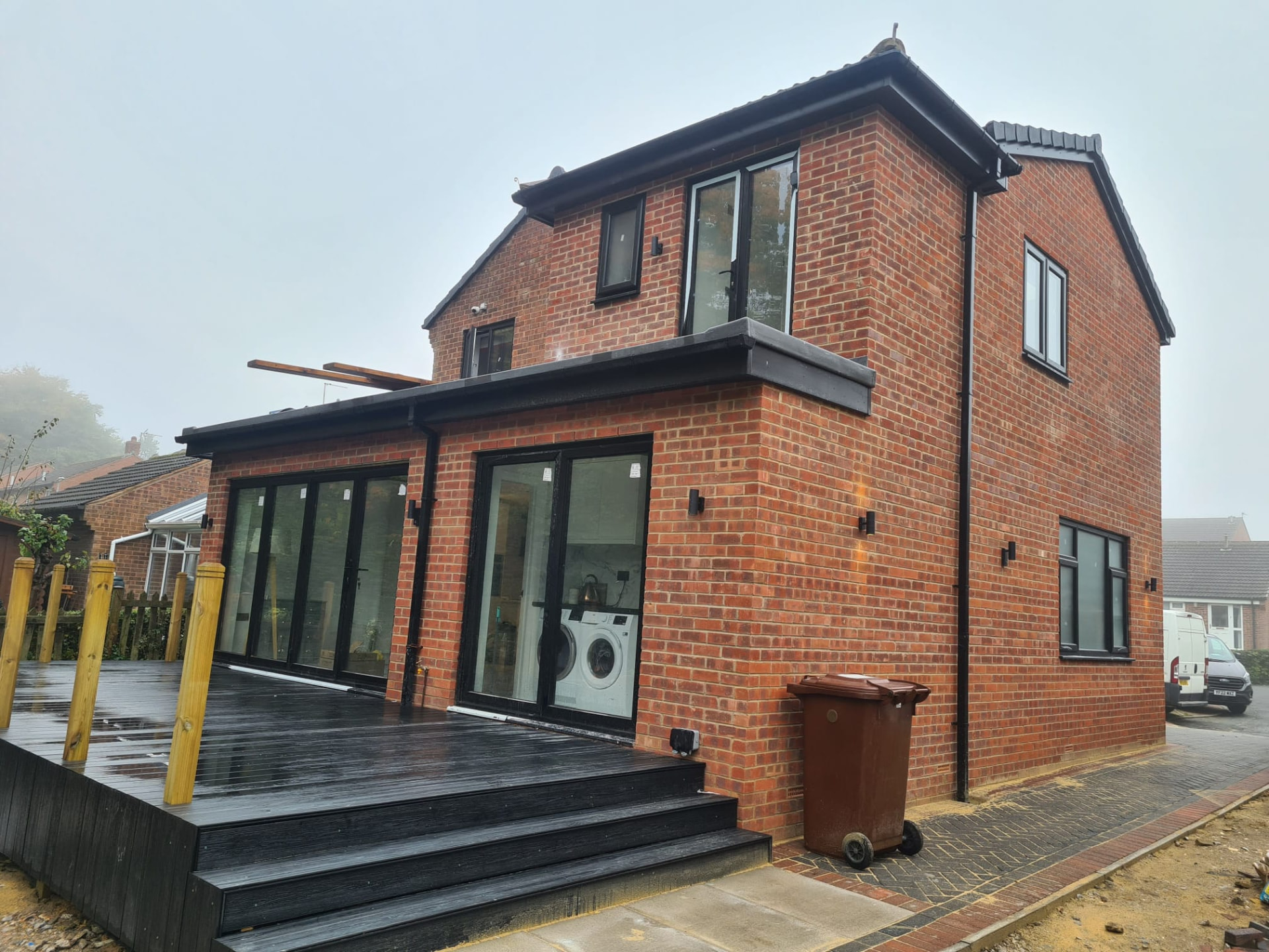 Completed side extension with dark grey window frames and a black timber deck, Leeds